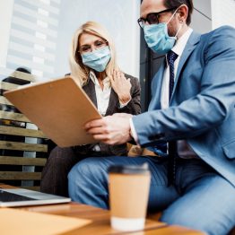 Dark-haired Caucasian man with a clipboard and a paper document sitting by his coworker outside